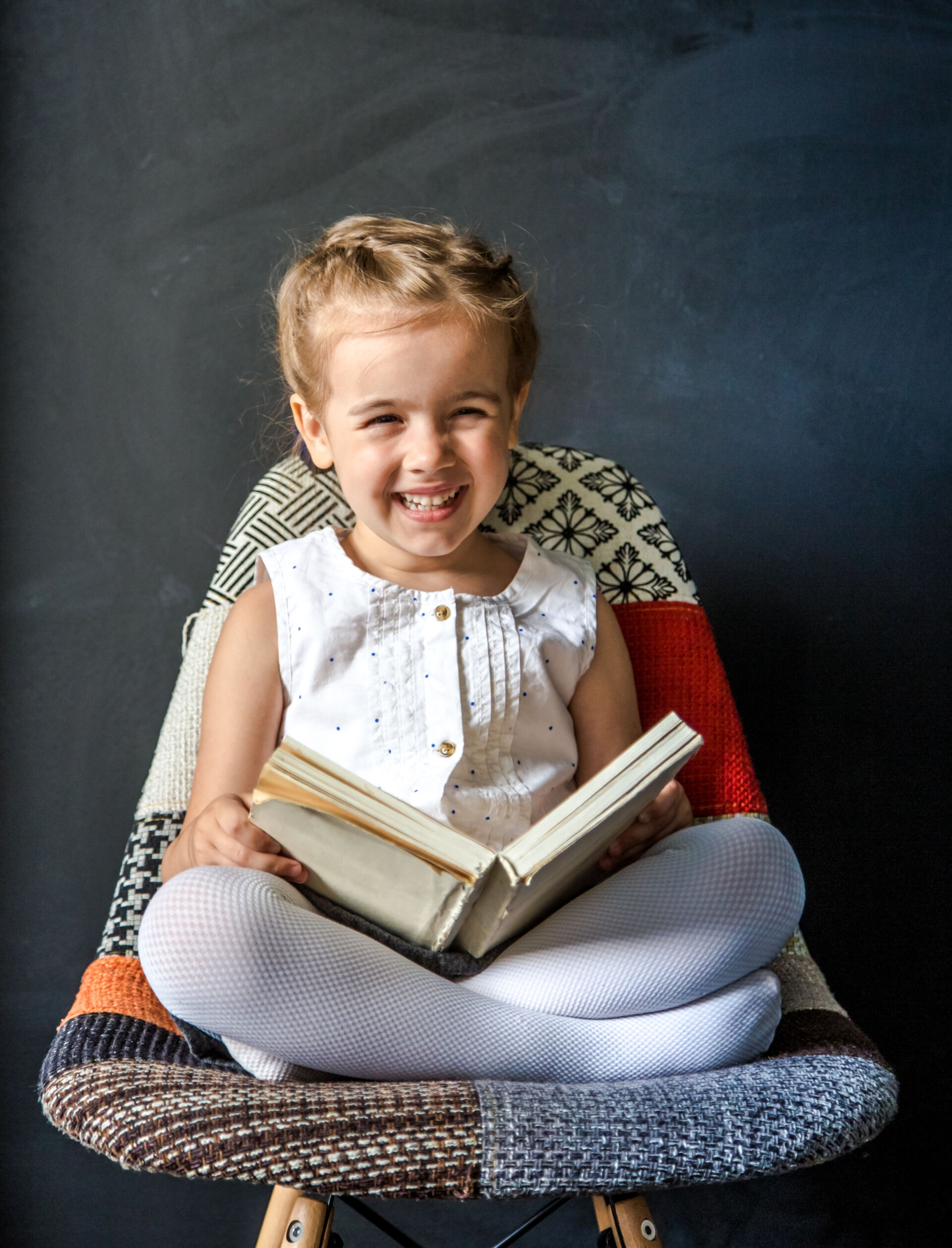 little girl sitting on a chair and reading a book